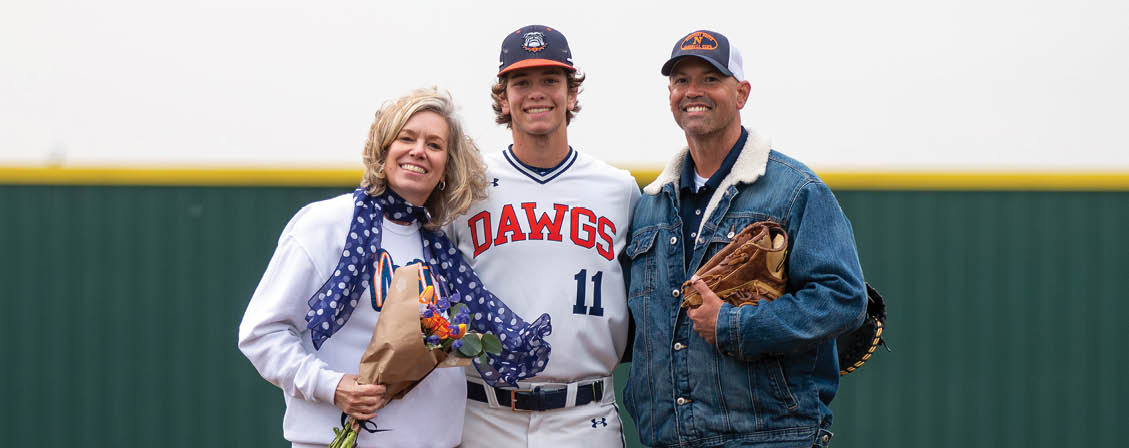 A man, woman, and another person pose on a baseball field. The man is wearing a baseball uniform and holding a baseball glove. The woman is holding a bouquet of flowers. Contenido generado con IA