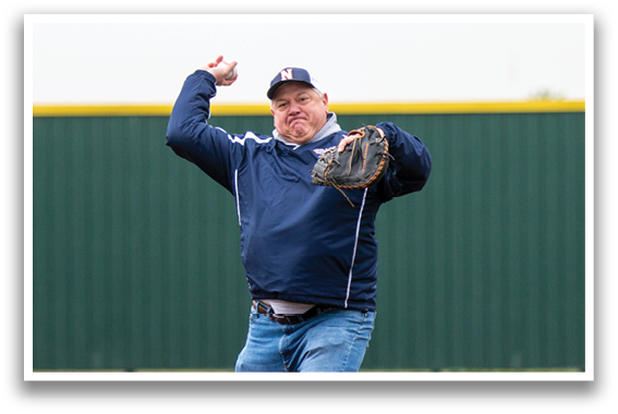 A man in a blue jacket is pitching a baseball on a field. Contenido generado con IA