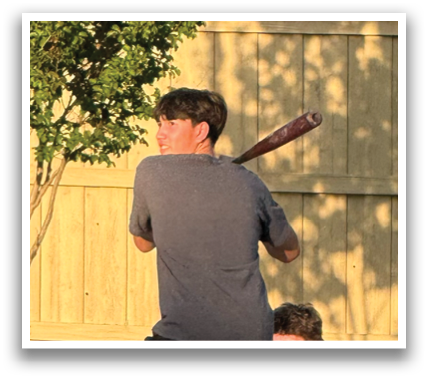 A group of young men are sitting on the sidewalk, watching a man swing a baseball bat. Contenido generado con IA