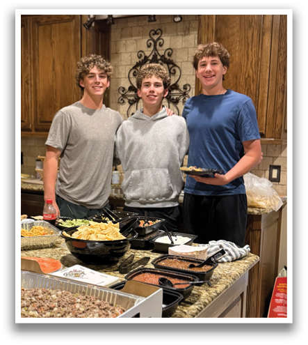 Three young men pose for a picture in a kitchen filled with food. Contenido generado con IA
