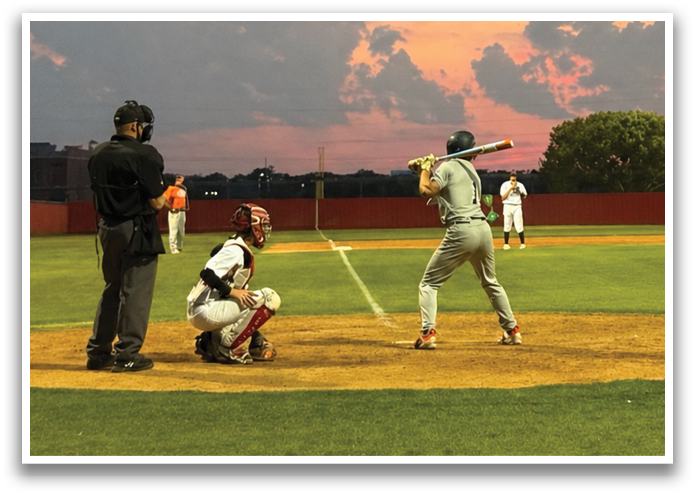 A baseball game is taking place with a batter holding a bat and a catcher ready to catch the ball. The sun is setting in the background, casting a warm glow on the field. Contenido generado con IA