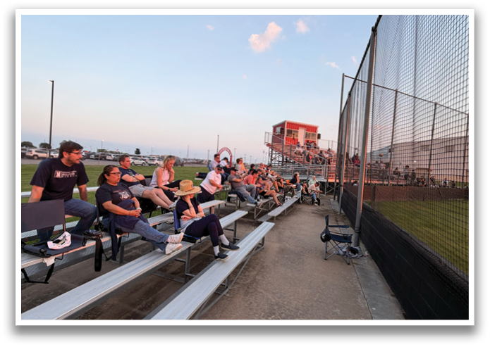 A group of people are sitting on a bench in a baseball field. Contenido generado con IA