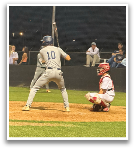 A baseball player is at bat, holding a bat and preparing to swing. The catcher and umpire are behind him, ready for the play. Contenido generado con IA