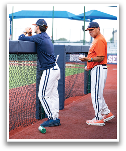 Two men are standing on a baseball field, one of them leaning on a fence. Contenido generado con IA