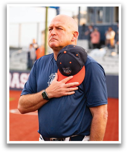 A man wearing a blue shirt and a blue hat stands on a baseball field. Contenido generado con IA