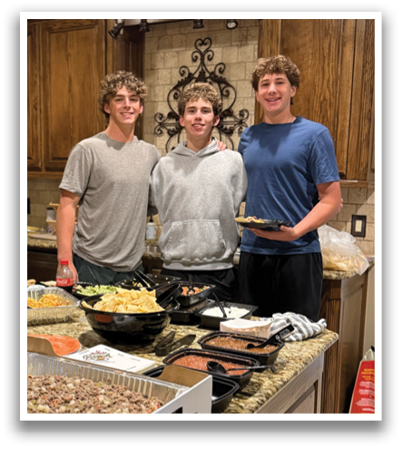 Three young men pose for a picture in a kitchen filled with food. Contenido generado con IA
