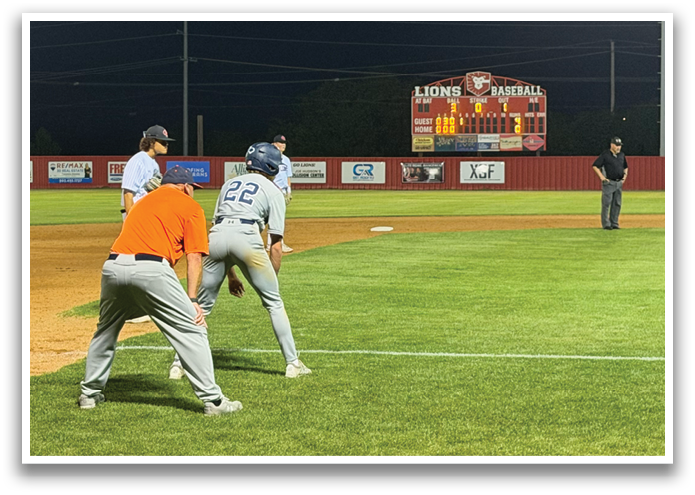 A baseball game is taking place on a field with players in action. A batter is swinging his bat, while a catcher is ready to catch the ball. There are several other players on the field, some of them wearing baseball gloves. The scene is illuminated by lights, creating a nighttime atmosphere. Contenido generado con IA