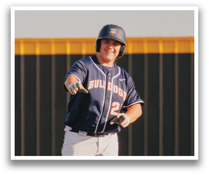 A baseball player in a blue jersey is standing on a field, holding a bat and smiling. Contenido generado con IA