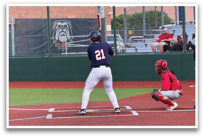 A baseball player is at bat, wearing a blue shirt and white pants. The catcher is positioned behind him, wearing a red shirt. A man in a red shirt is sitting in the stands, watching the game. Contenido generado con IA