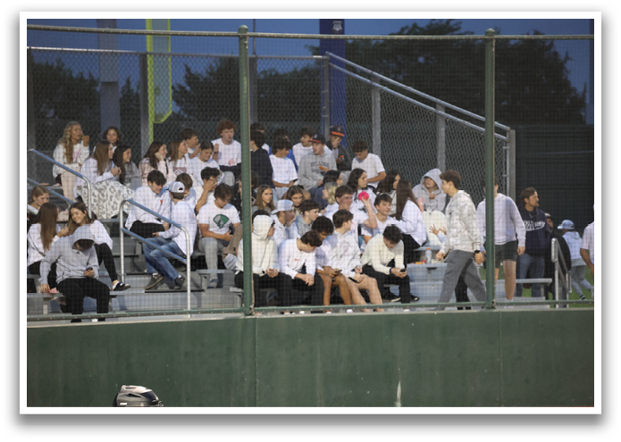 A group of people are sitting on a bench, watching a baseball game. Contenido generado con IA