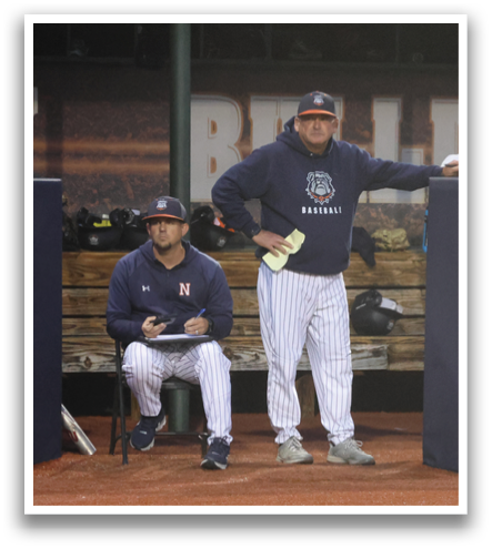 Baseball players are standing on a field, some of them wearing helmets. A man is sitting on a bench, watching the players. Contenido generado con IA