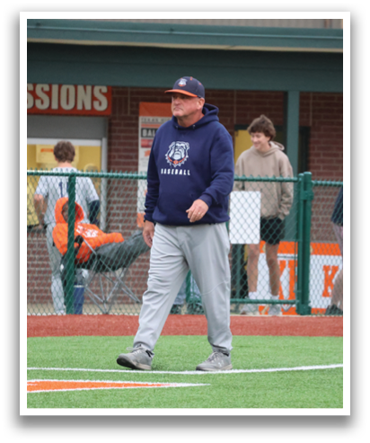 A man in a blue hoodie stands on a baseball field, talking to another man. Contenido generado con IA