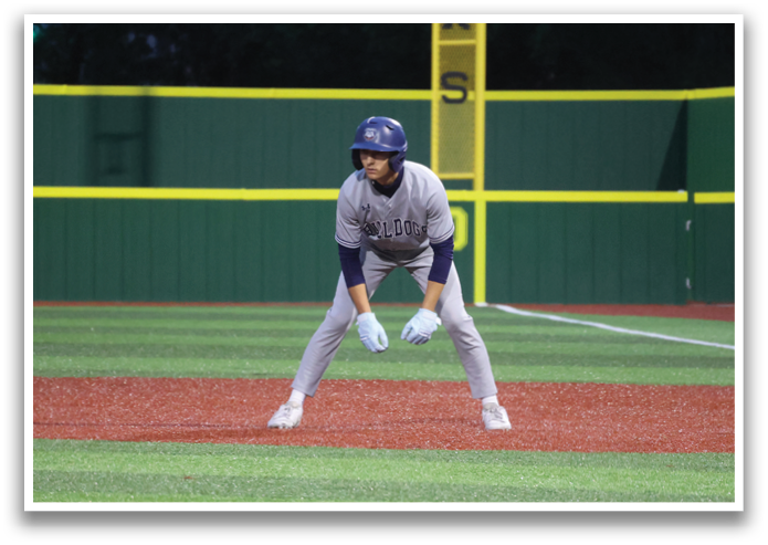 A baseball player is standing on the field, wearing a helmet and holding a bat. Contenido generado con IA
