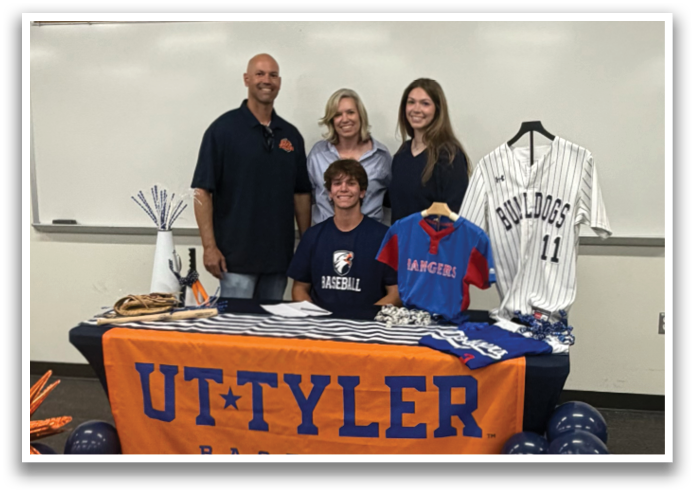 A group of people, including a young boy, pose for a picture in front of a table with a UT Tyler baseball banner. Contenido generado con IA