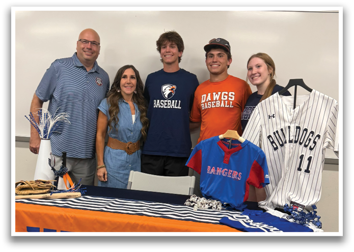 A group of people pose for a photo in front of a table with a UT Tyler baseball jersey and a shirt on it. Contenido generado con IA