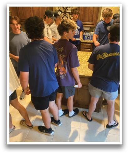 A group of people are standing in a room, some of them wearing blue shirts. They are gathered around a table, and there is a bottle on the table. Contenido generado con IA