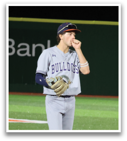 A baseball player stands on the field, wearing a grey uniform and a blue hat. He is holding his glove and appears to be looking up at the scoreboard. Contenido generado con IA