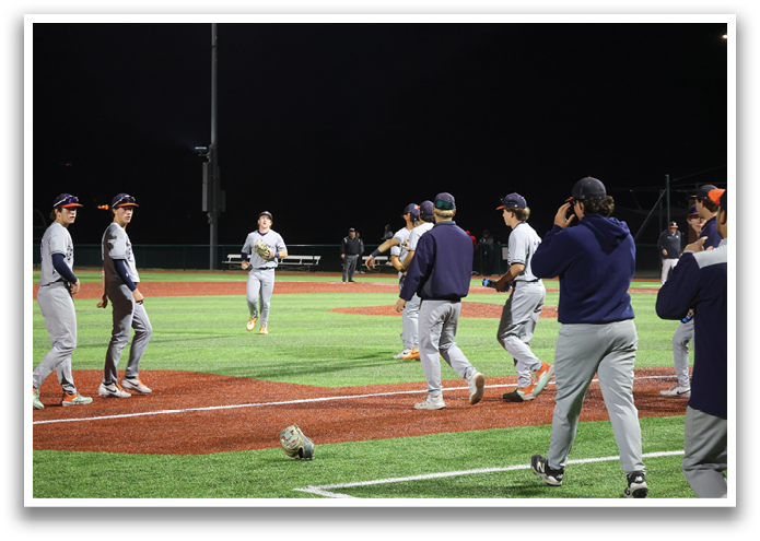 A group of baseball players on a field, some of them wearing blue and white uniforms. One player is holding a baseball bat, and another player is holding a baseball glove. The players are standing around the home plate, possibly discussing their game strategy or taking a break. Contenido generado con IA