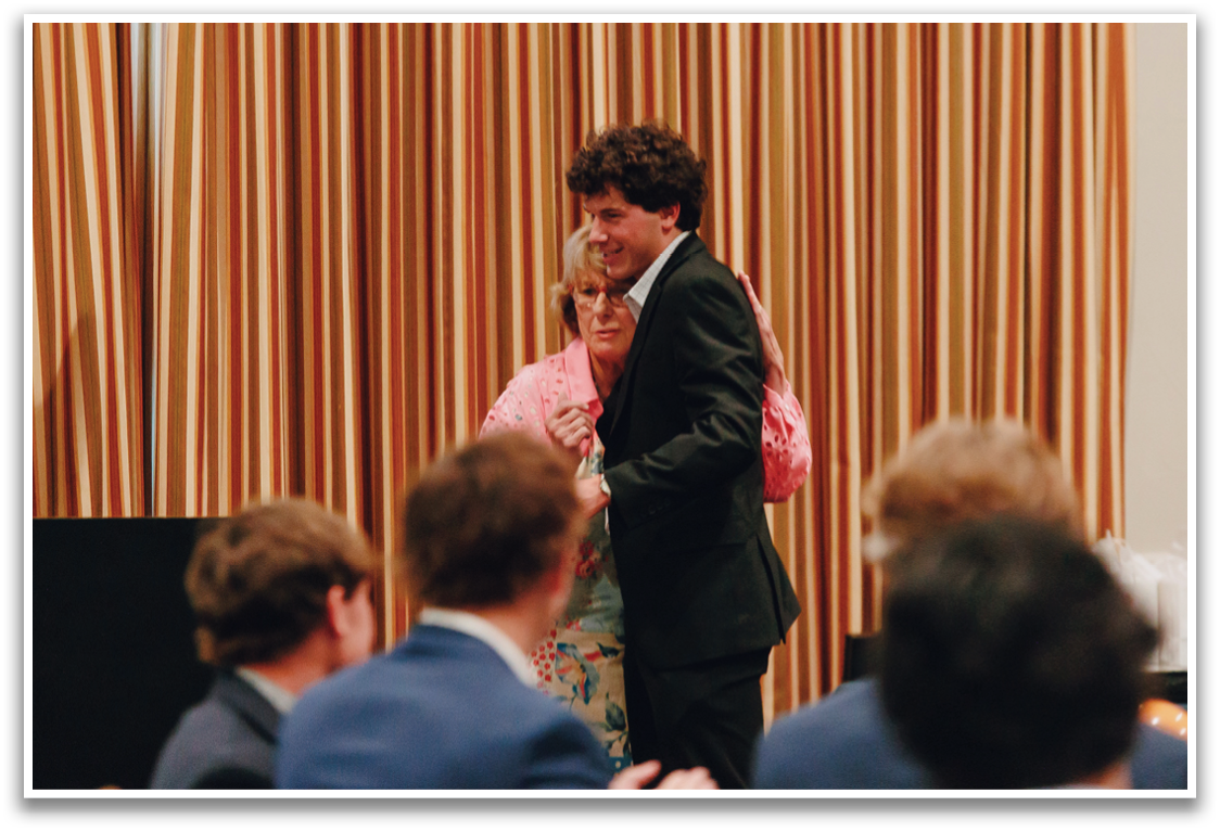 Two people are standing in front of a crowd, shaking hands. Contenido generado con IA