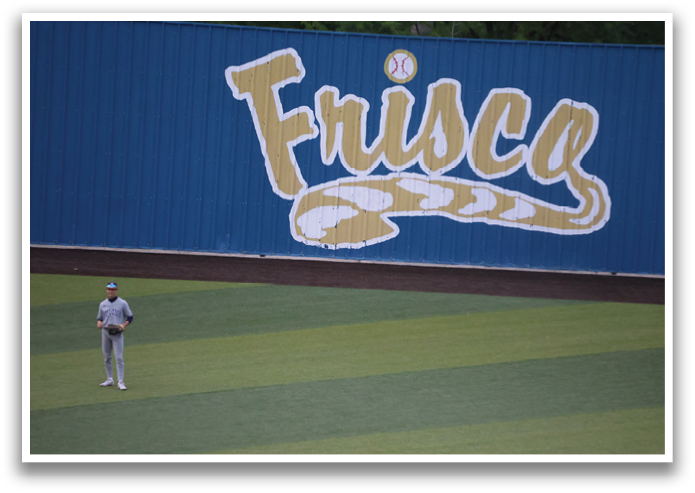 A baseball player stands on a field with a blue wall in the background. Contenido generado con IA