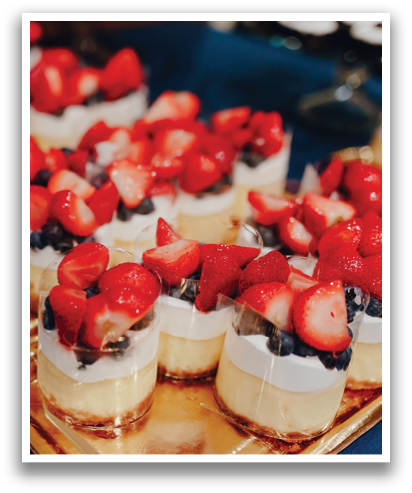 A table with a tray of desserts, including strawberries and blueberries, and a glass of wine. Contenido generado con IA