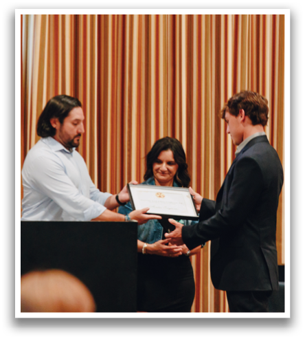 A man and woman are receiving awards at a ceremony. The man is wearing a suit and shaking hands with the woman. Contenido generado con IA