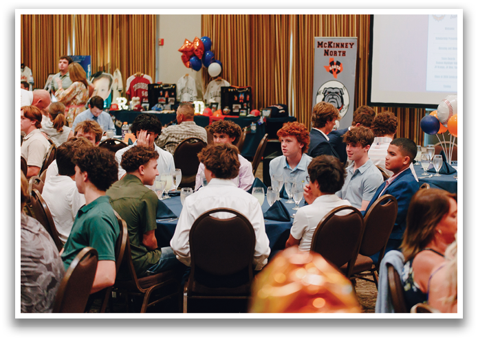 A group of people are sitting at tables in a room, with some of them wearing ties. The tables are set with plates, cups, and forks. There are also balloons in the room, and a TV screen is visible in the background. Contenido generado con IA