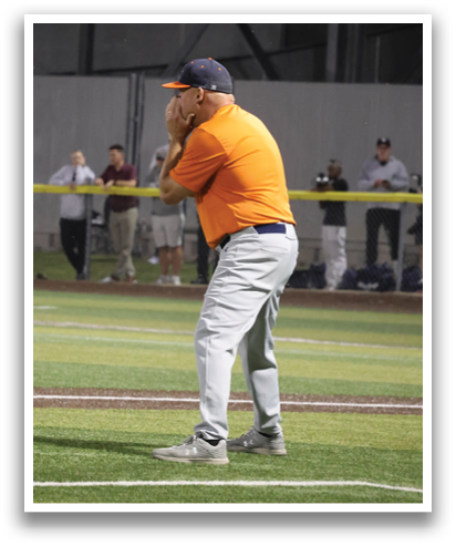 A man in an orange shirt is standing on a baseball field, holding a baseball bat and preparing to swing. Contenido generado con IA
