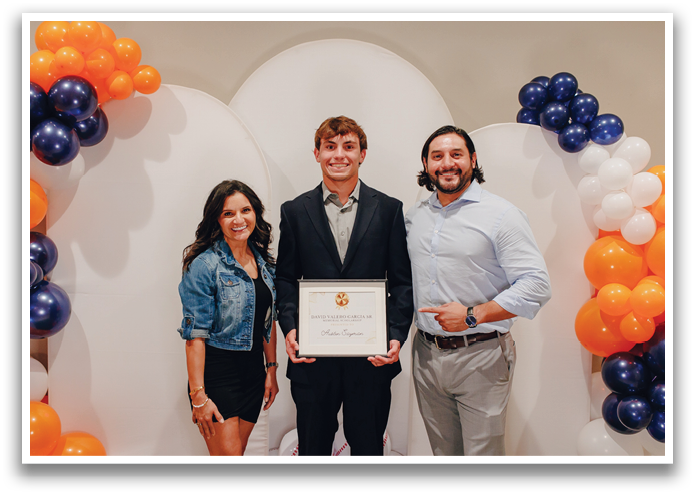 A man and two women pose for a picture in front of a white backdrop. The man is holding a certificate while the women stand beside him. Contenido generado con IA