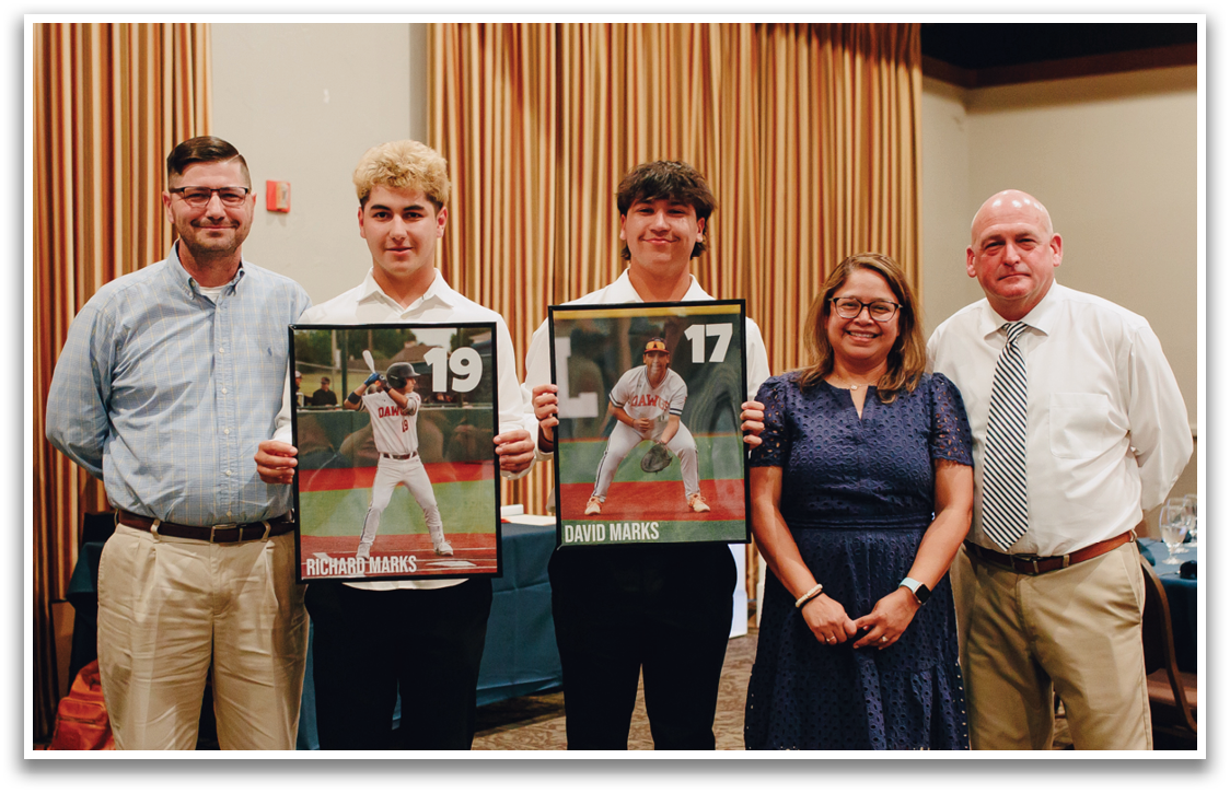 A group of people pose for a photo with two framed pictures of baseball players. Contenido generado con IA