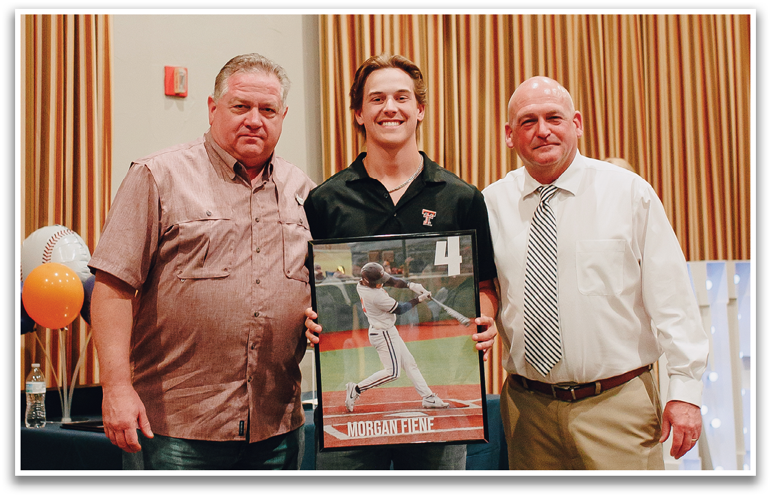 Three men are standing next to each other, posing for a photo. One of the men is holding a framed item, possibly a baseball or a photo of a baseball player. The men are dressed in business attire, with one wearing a tie. The setting appears to be a formal event or a conference. Contenido generado con IA