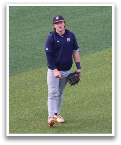 A baseball player in a blue shirt and white pants is standing on a green field. Contenido generado con IA