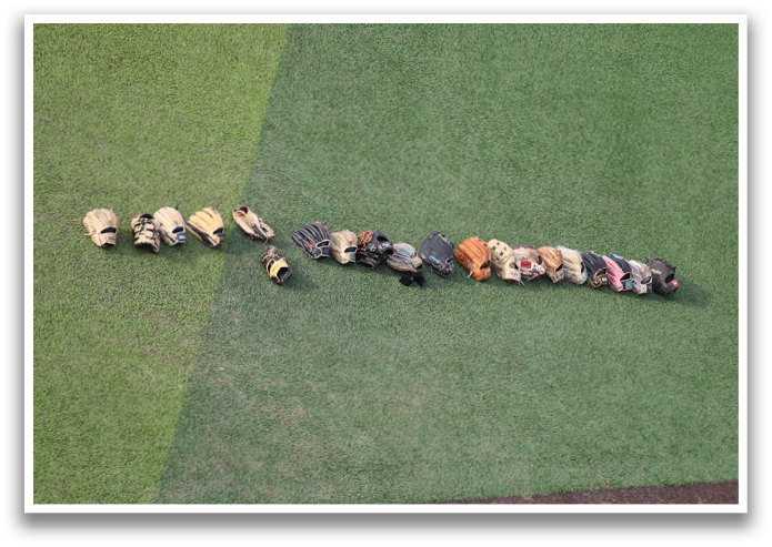 A row of baseball gloves and bags are lined up on a green field. Contenido generado con IA