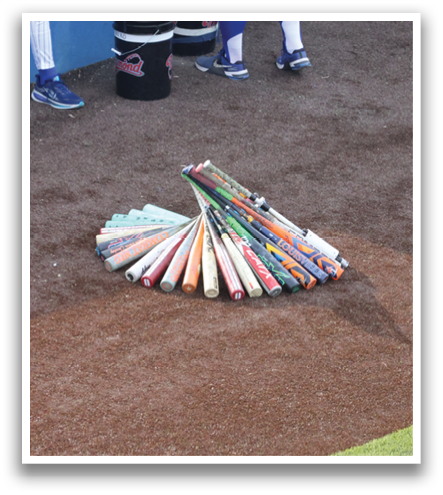 A group of baseball players are standing on a baseball field. There are several baseball bats on the ground, with some of them leaning against a wall. Contenido generado con IA