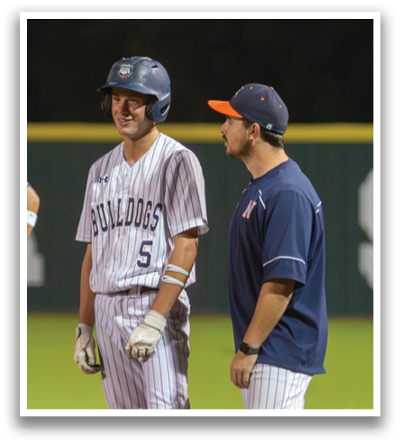 Two baseball players are standing on the field, one wearing a blue shirt and the other wearing a red shirt. They are talking to each other. Contenido generado con IA