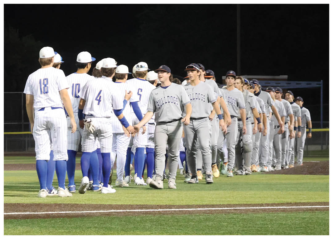 Baseball players in uniforms are lined up on the field, some wearing blue and white. A man in a black shirt is standing next to them, possibly a coach or an umpire. The scene appears to be taking place at night. Contenido generado con IA