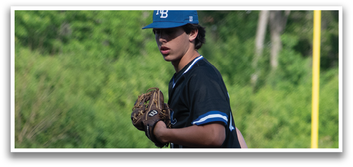 A baseball player in a black shirt and blue hat is standing on a pitcher's mound. Description generated by AI