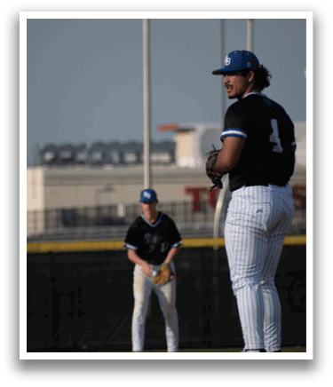 A baseball player wearing a black shirt and white pants stands on a field. Description generated by AI