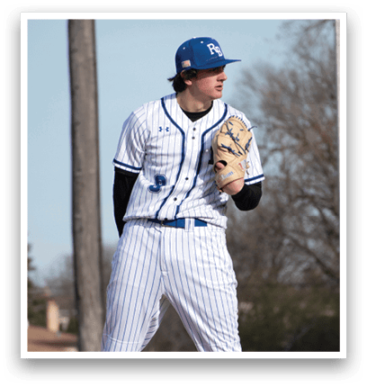A baseball player wearing a blue hat and white uniform stands on a mound of dirt. Description generated by AI