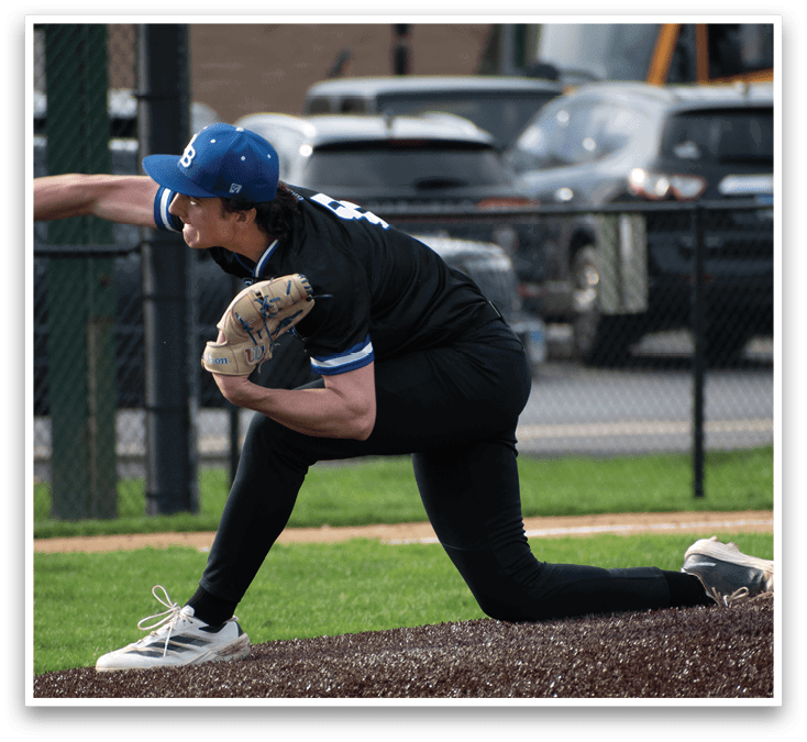 A baseball player in a black shirt and blue hat is in a crouched position on the field. Description generated by AI