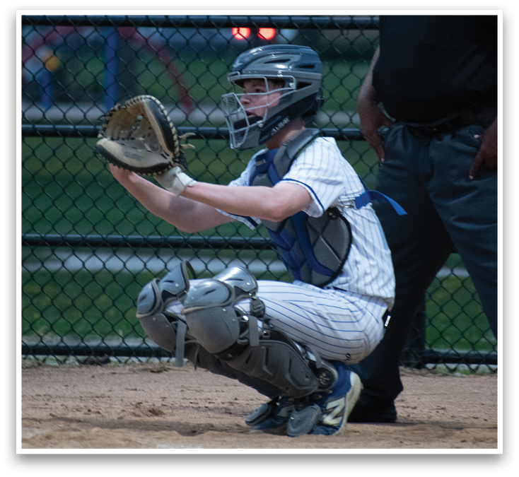 A baseball catcher wearing a blue shirt and white pants. Description generated by AI