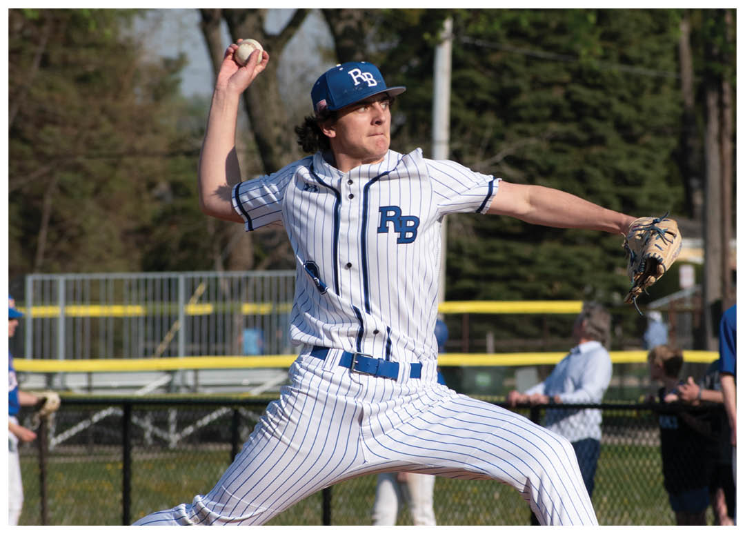 A baseball player in a white and blue uniform is pitching a ball. Description generated by AI