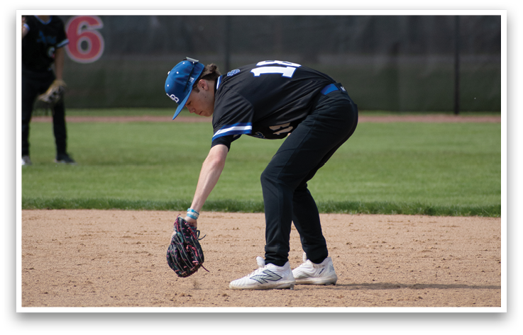 A baseball player wearing a blue hat and black shirt bends over to catch a ball. Description generated by AI