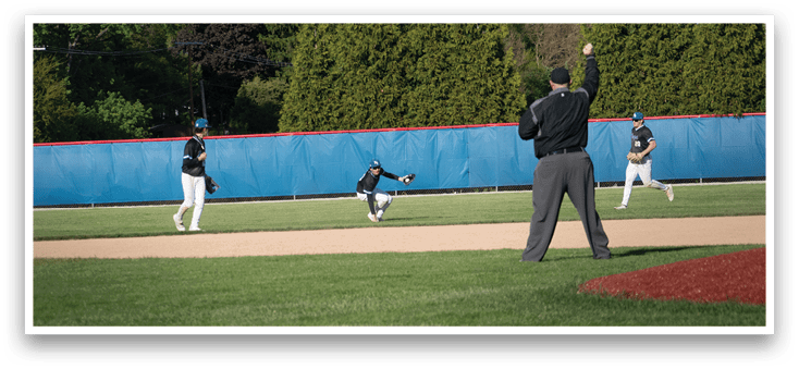 A baseball game is taking place on a field with a man in a black shirt and gray pants standing behind a catcher. Description generated by AI