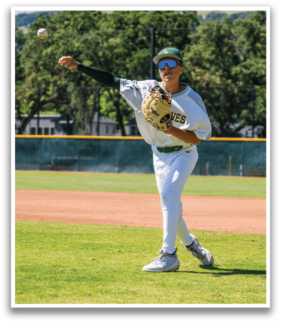 A baseball player wearing a white uniform and green hat is throwing a ball. Description generated by AI