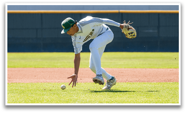 A baseball player in a green and white uniform is bending over to catch a ball. Description generated by AI