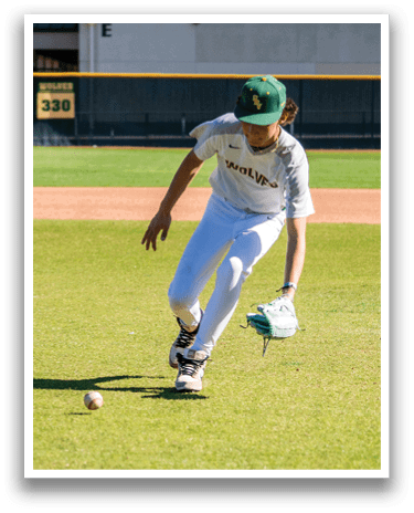 A baseball player in a white uniform is bending over to catch a ball on a field. AI generated content
