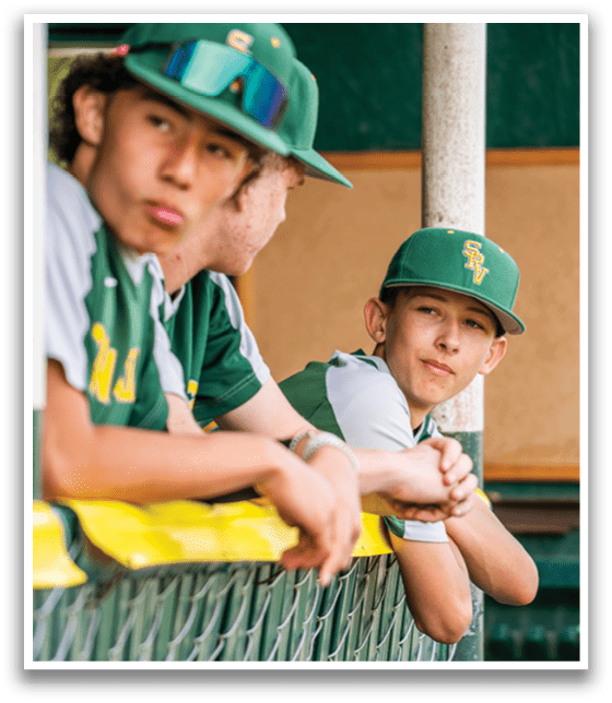 Two boys wearing baseball caps and jerseys are sitting on a bench. AI generated content
