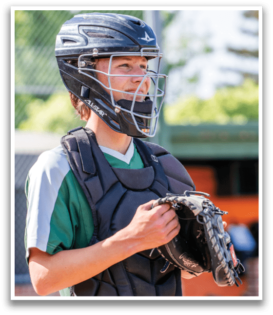 A young man wearing a baseball helmet and chest protector is smiling. AI generated content