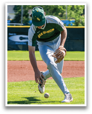 A baseball player wearing a green and white uniform is bending over to catch a ball. Description generated by AI